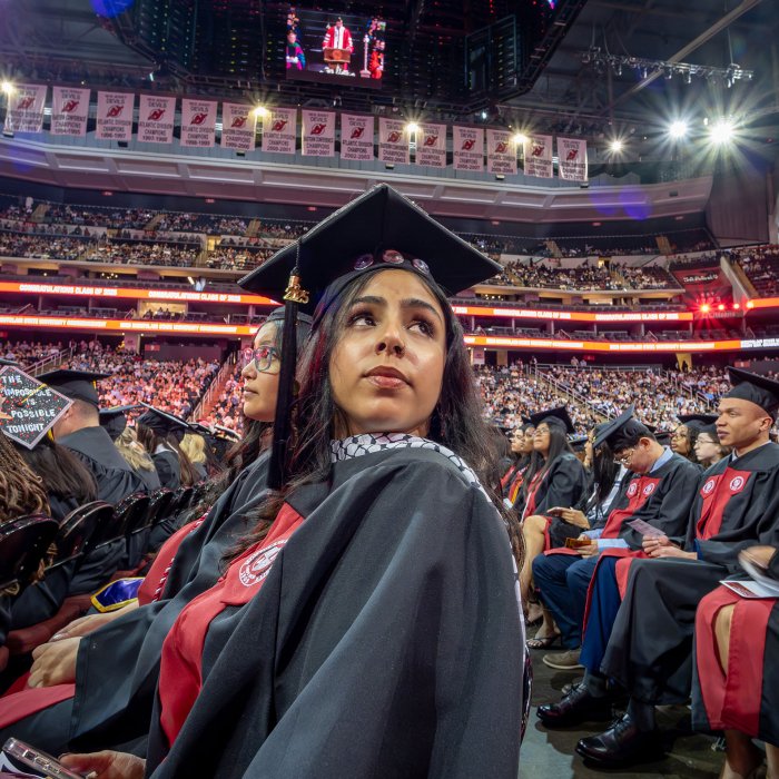 a graduate seated among peers looks toward the stands 