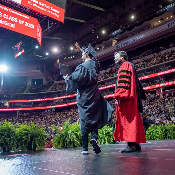 President Koppell stands next to a graduate waving on stage