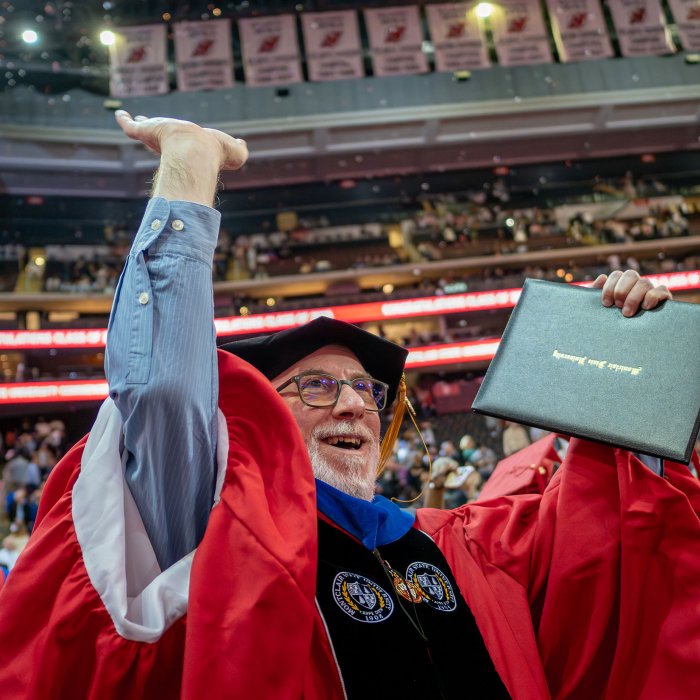 Doctoral graduate smiling with arms up, holding diploma holder