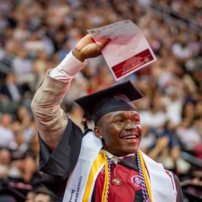A graduate with hands up, waving a program