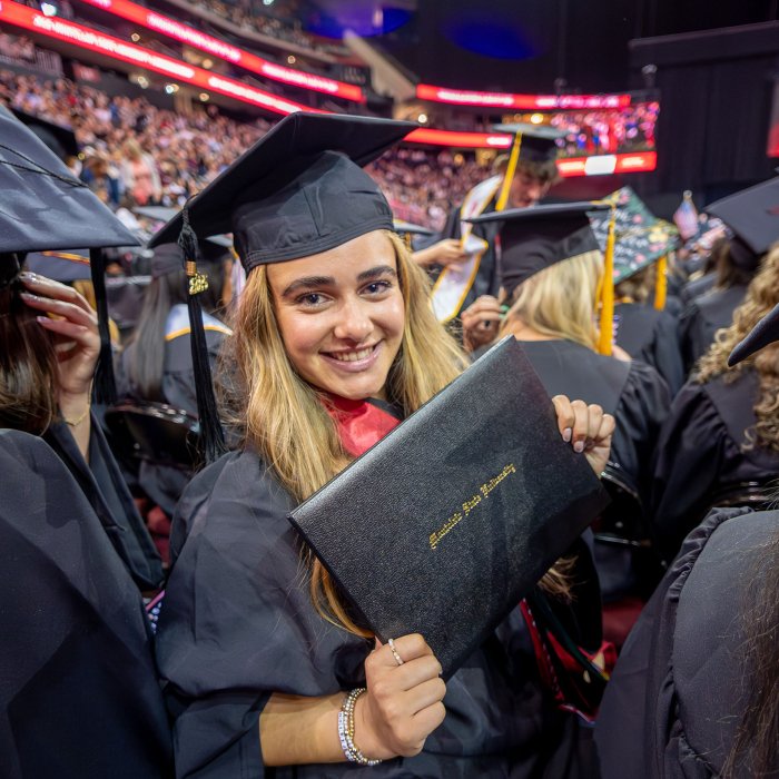graduate in black cap and robe showing diploma holder