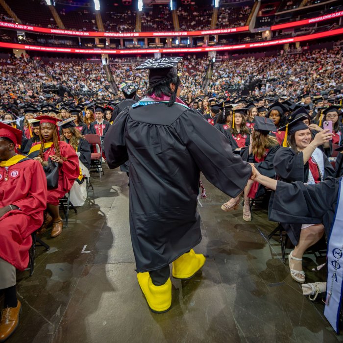 Graduate student walks down the aisle wearing the talons of Rocky, Montclair's mascot