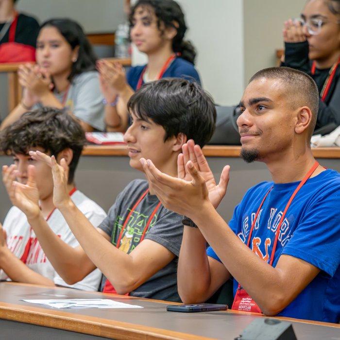 Group of students in a classroom applauding while listening. 