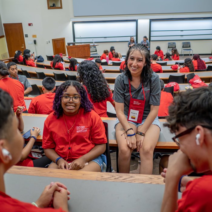 HSCI students in a classroom smiling and conversing with one another, wearing red shirts.