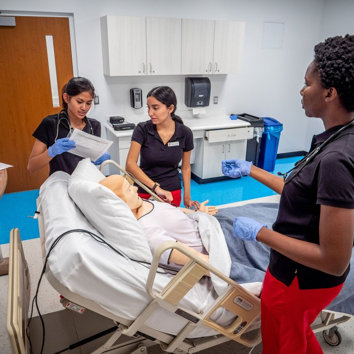 Three nursing students around a simulation dummy in a hospital bed