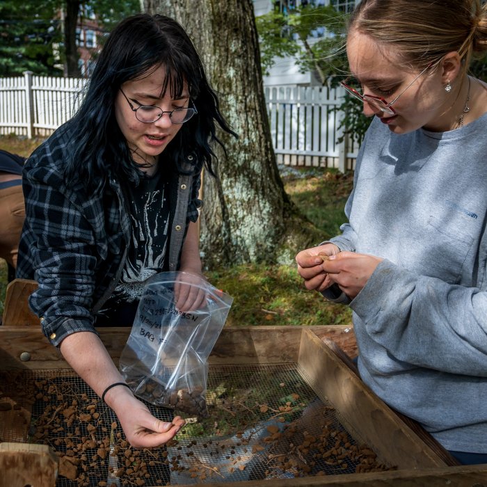 Two students examine soil samples over a soil screener.