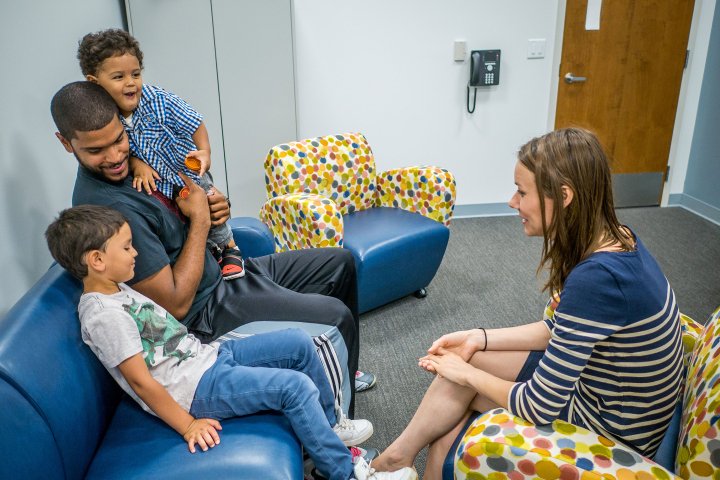 An adult sitting on couch with two children, across from another adult