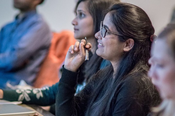 A woman smiles and holds a pen while taking notes in a classroom