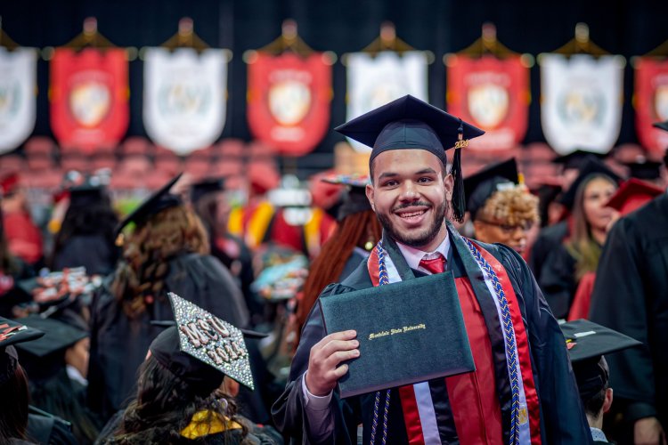 A graduate in cap and gown celebrates at a Montclair State University commencement ceremony, showing off a diploma.