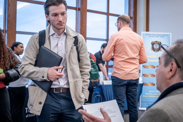A student holding a portfolio talks with a recruiter at a career fair.