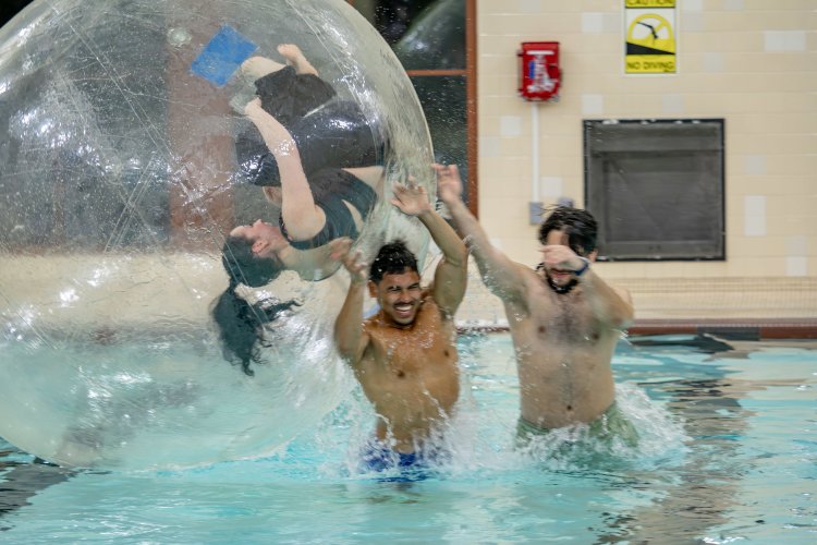 Students play in the Recreation Center’s pool. One student is rolling inside a large, inflatable plastic sphere on the surface of the water. 