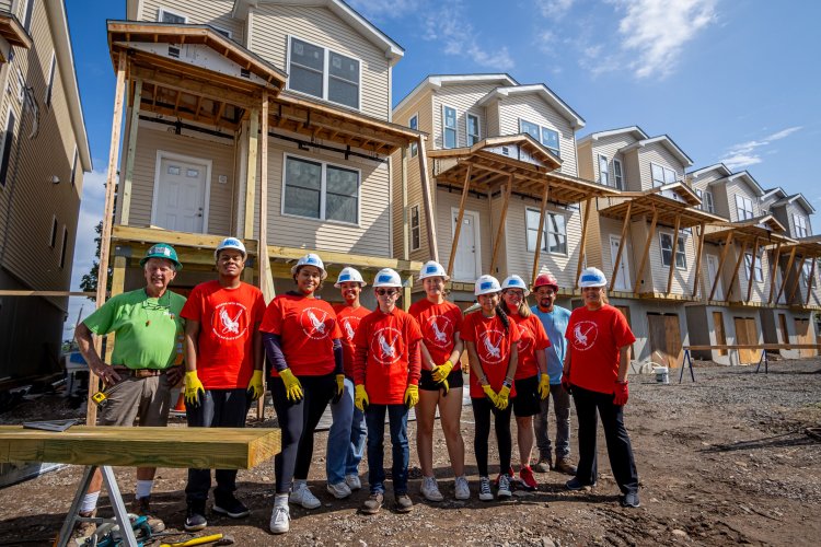A group of 10 people, including students and building supervisors, stand at a construction site of new housing.