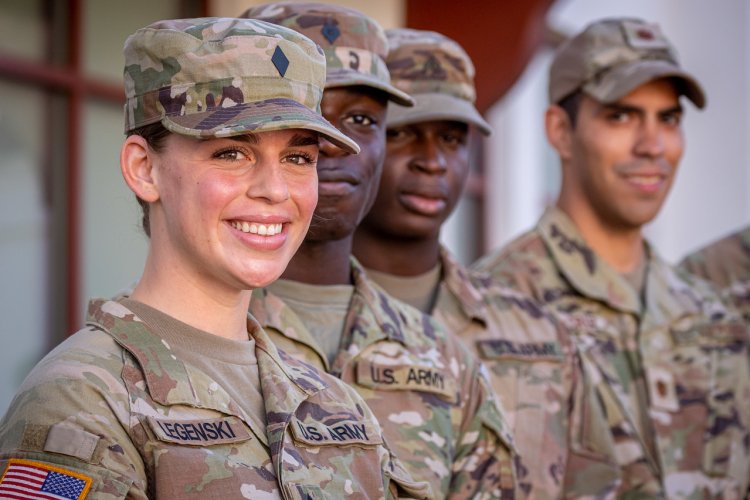 Several U.S. Army soldiers in camouflage uniforms and caps stand in formation outdoors. 