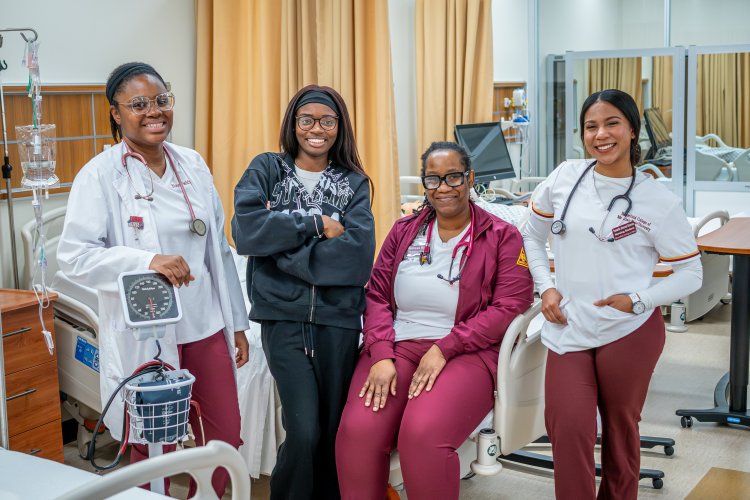 Four women smiling at the camera with their scrubs and nursing gear on. 