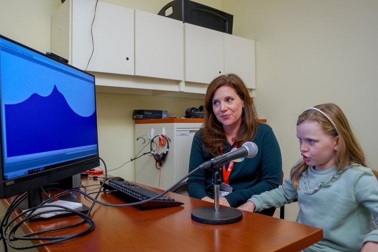 8-year-old Colette Fougere says ‘r’ into a microphone while Alexis Gallagher looks on.