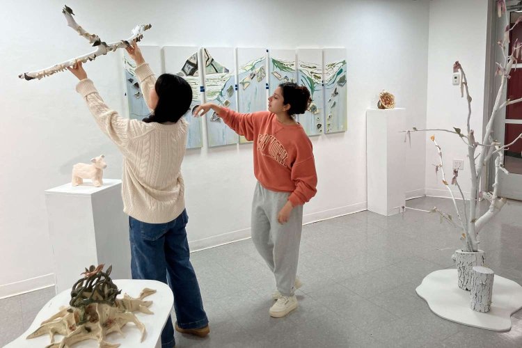 Two students in a gallery, one student holding a sculpture up.