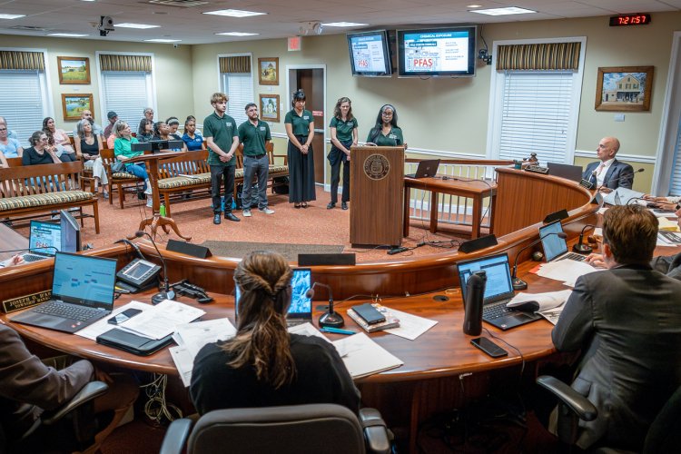 Montclair Green Teams students present their sustainability project at a Verona, New Jersey town meeting, standing at a podium before a curved council table and seated audience.