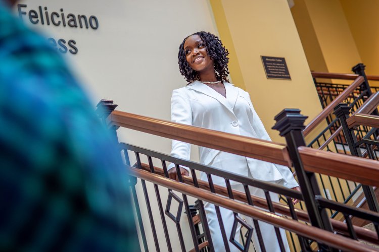 Graduate walking down stairs of Feliciano School of Business. They are smiling while looking away from the camera.
