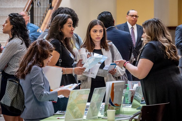 Three females are at a table listening closely to another woman explaining something to them.