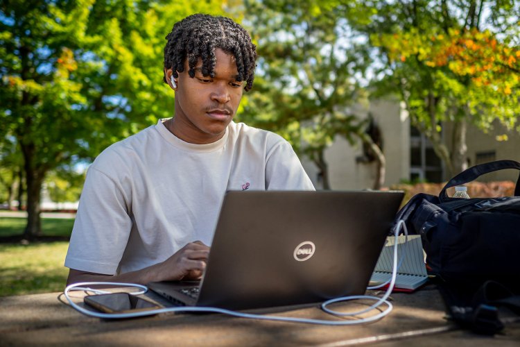 Student working on their laptop outside near Montclair State Univerisity quad.