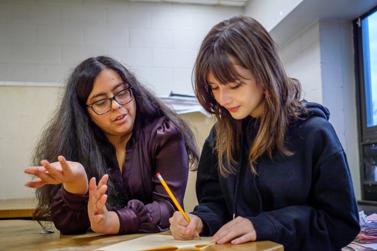 A teacher and a student are talking while the student is writing something down.