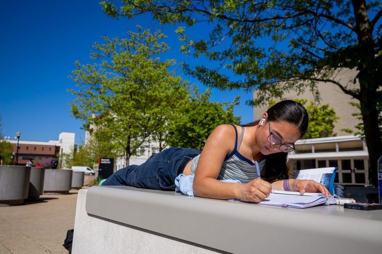 A student writes in a notebook outdoors.