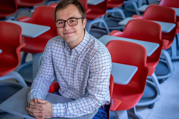Jacob Roby sits in a classroom full of red chairs.