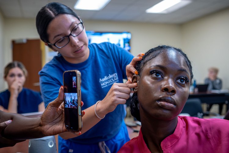 An audiology student fits another student with a hearing aid during a telehealth demonstration. 