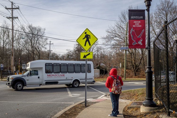 Student standing on a sidewalk as a Montclair State University shuttle drives by.