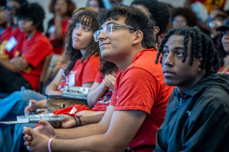 Franco Leon, wearing a red EOF T-shirt sits with hands clasped, smiling and looking up attentively during a conference session.