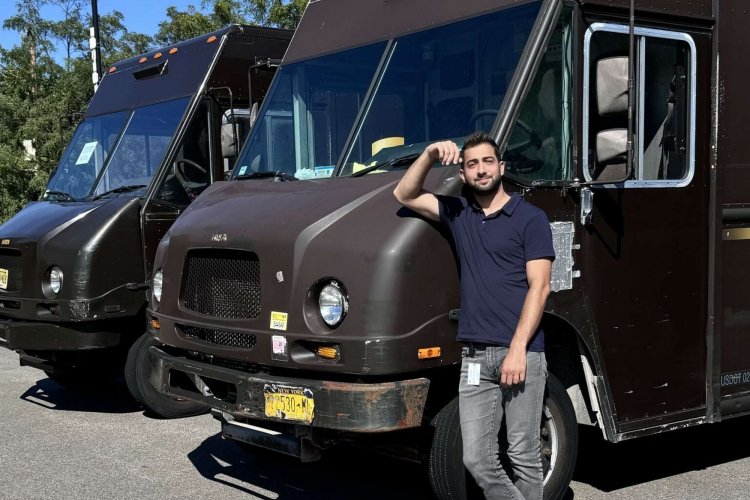 Man posing in front of two brown delivery trucks