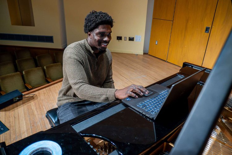 Student on stage at piano with computer.