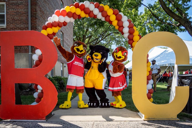 Mascots, Rocky, Deacon, and Roxy, pose under a balloon arch. The intials BC are propped up on the right and left side of the Mascots