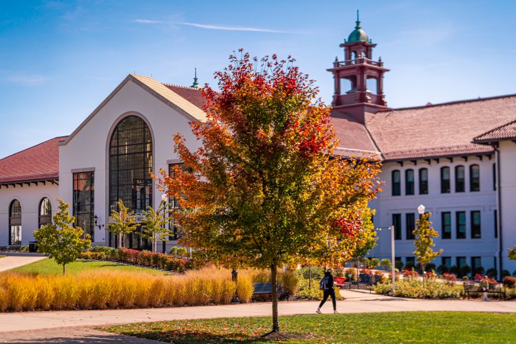 A student walks past Susan A. Cole Hall on Montclair State University’s campus as trees display colorful fall foliage.