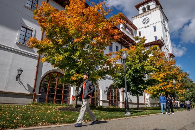 Students walking under trees with orange leaves in fall, outside of University Hall