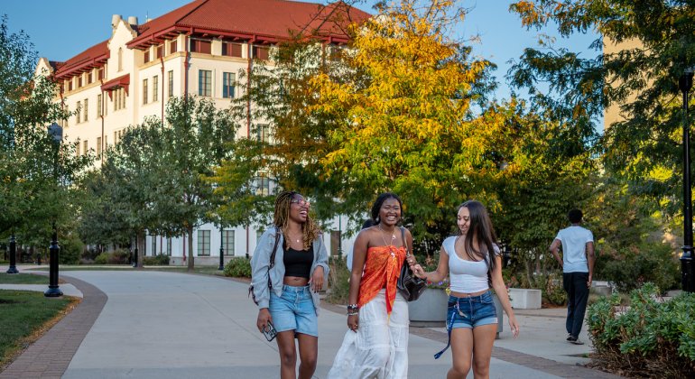 Three female students walking around campus laughing and conversating.