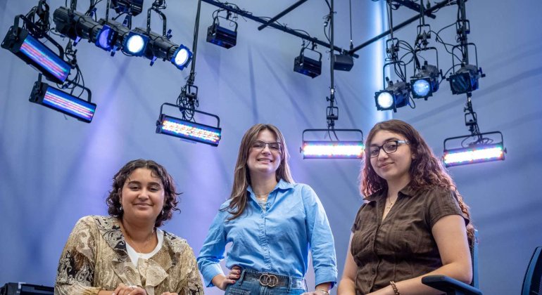Three students smile under set lights