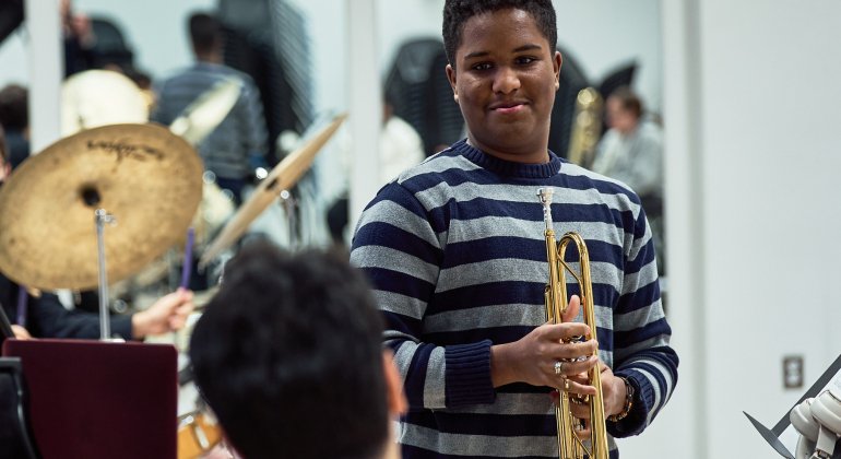 Pathways student with a trumpet speaking to a professor