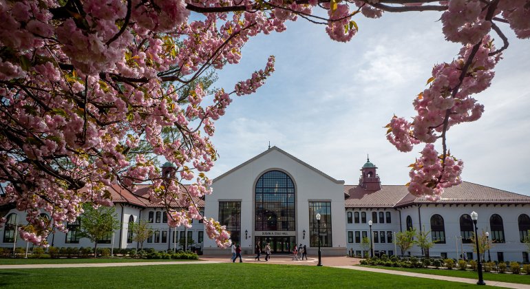 Wide shot of Susan A. Cole Hall with a couple of students walking by. There are cherry blossoms in the foreground.