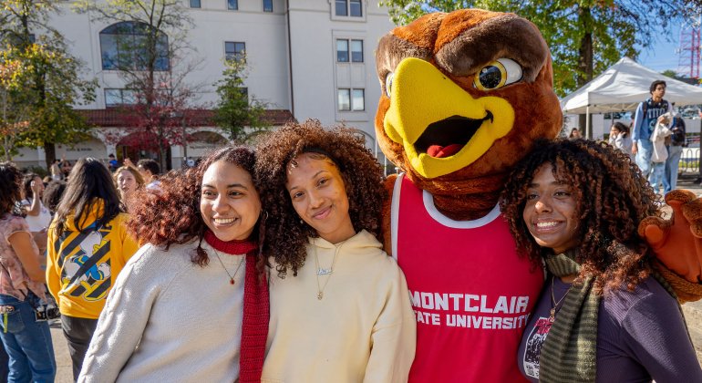 Three students taking a photo with Rocky.
