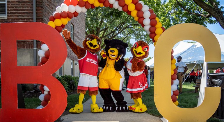 Mascots, Rocky, Deacon, and Roxy, pose under a balloon arch. The intials BC are propped up on the right and left side of the Mascots