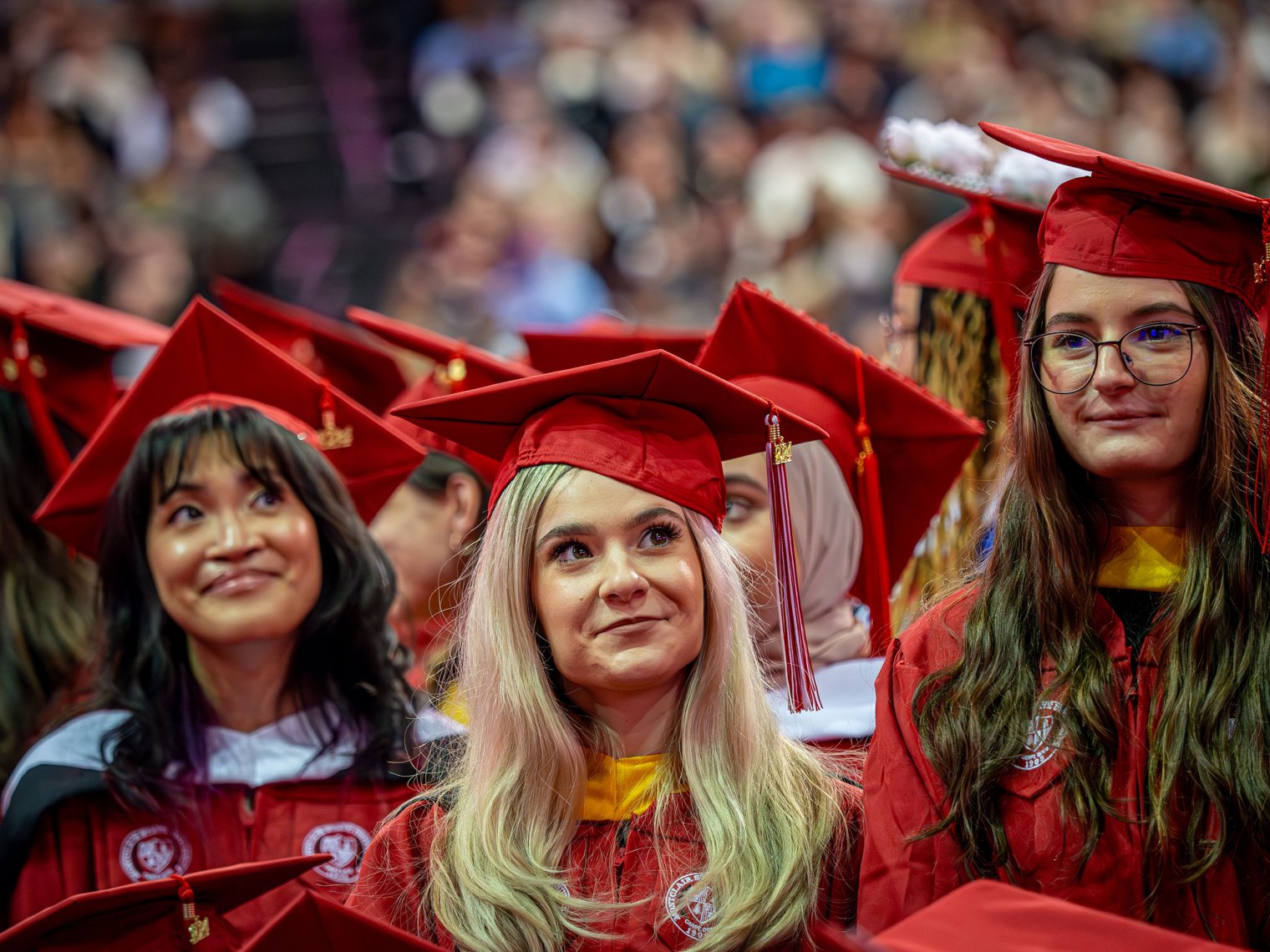 Three women in red cap and gown clothing at a commencement ceremony. 
