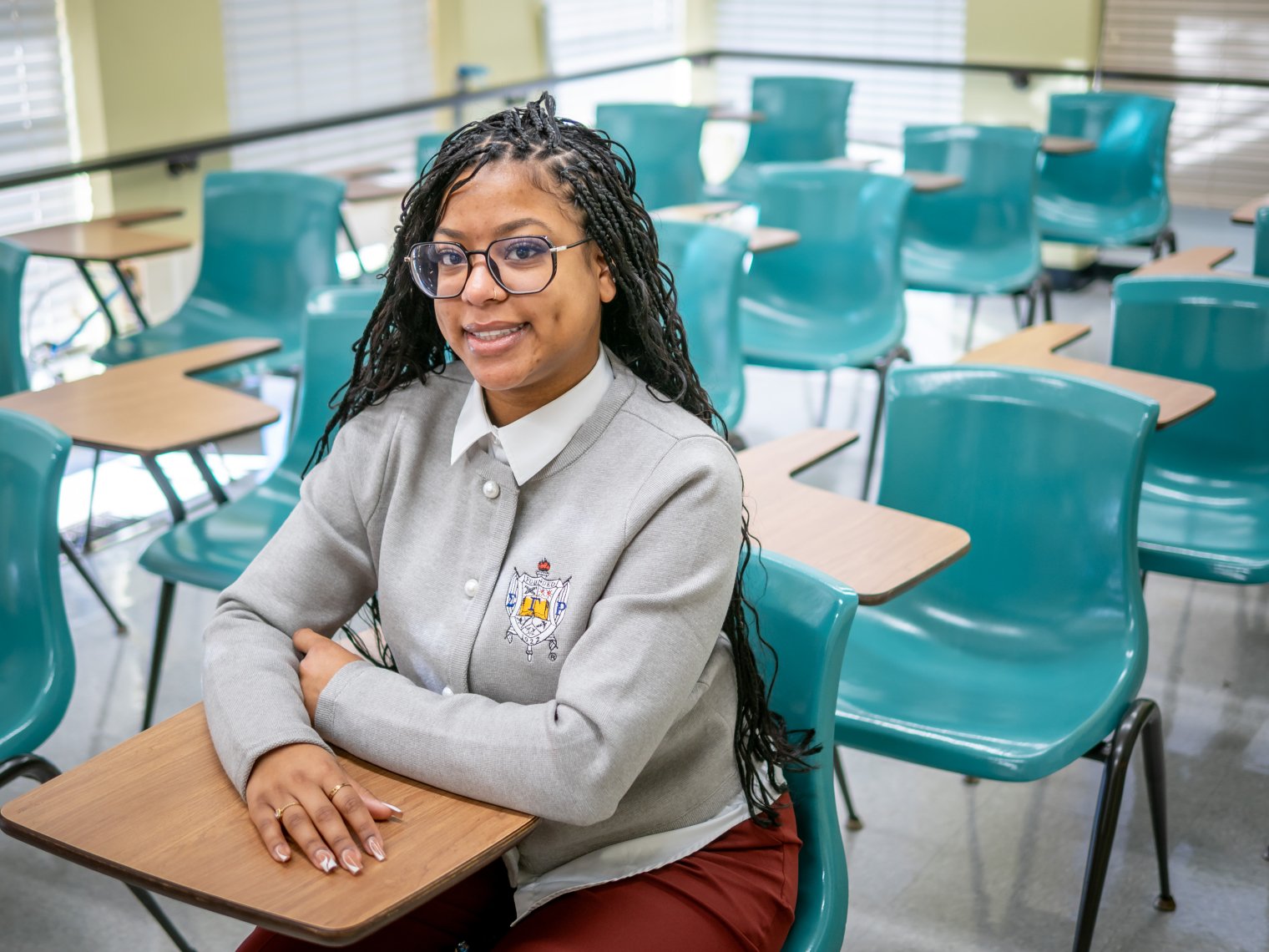 Woman is sitting in an empty classroom smiling. 