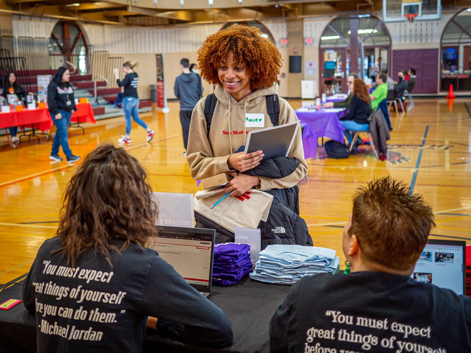 Student talks with two people seated at a table.