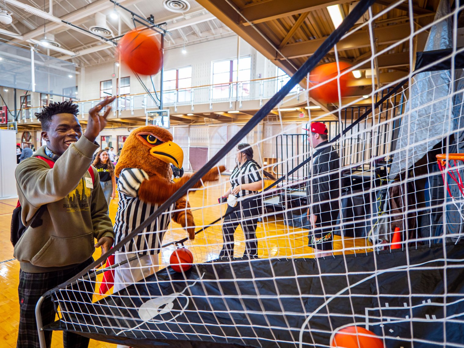 Male student shoots basketball alongside college mascot.