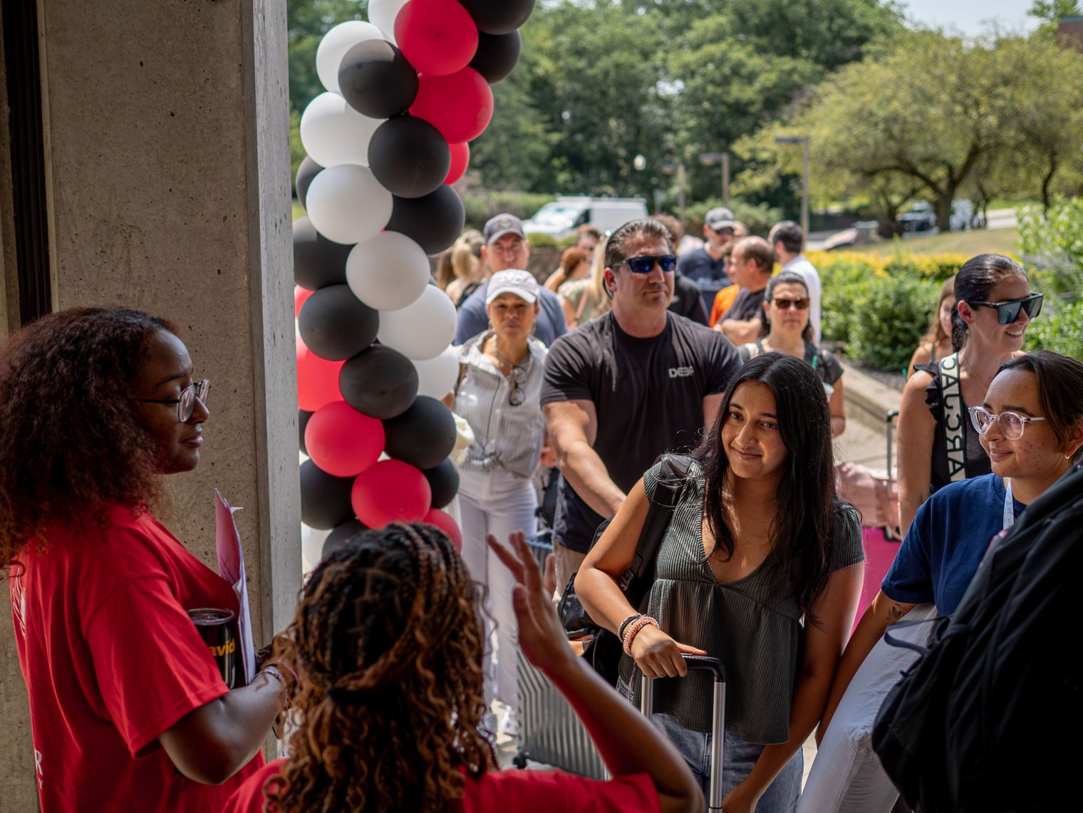 A line of high school students and their parents walk past balloons as they move into residence halls, experiencing campus life firsthand.