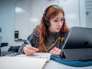 A student is taking notes while looking at her iPad while taking notes.