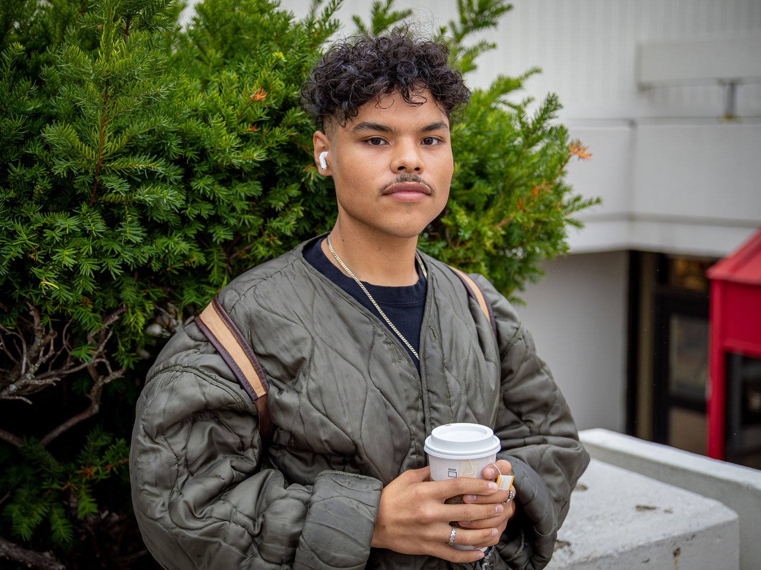 Jhonny Moncada stands on campus holding a paper coffee cup.