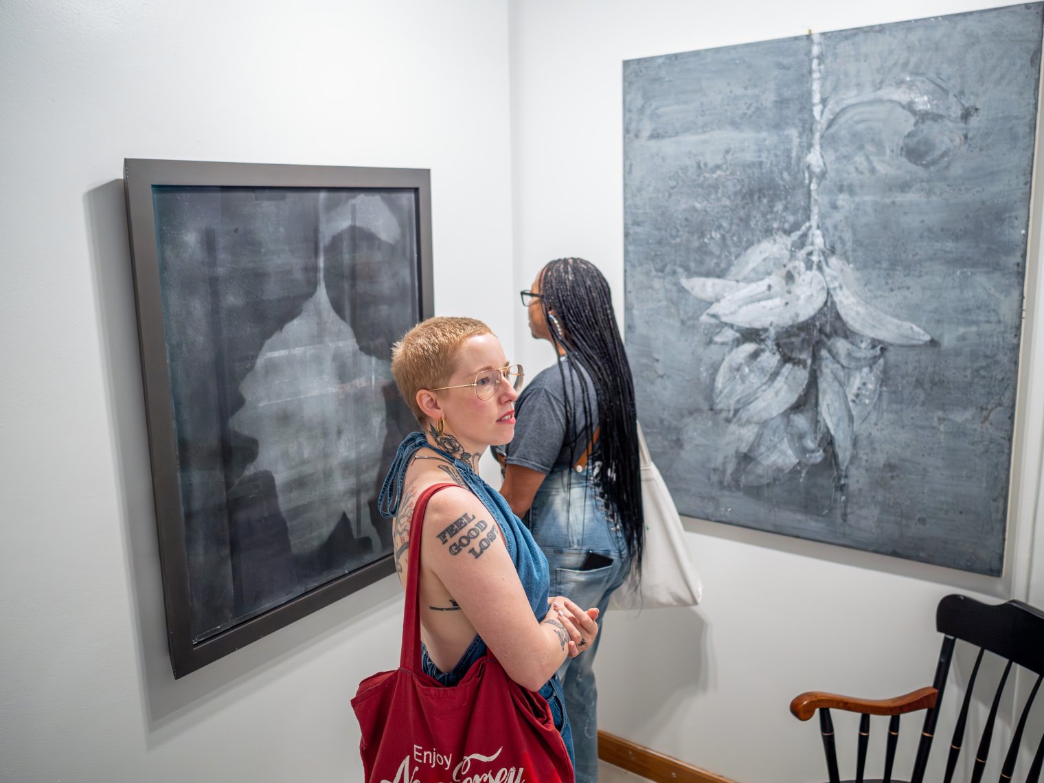 Two women are pictured looking over paintings, one one is intensely examining a black and white painting. 
