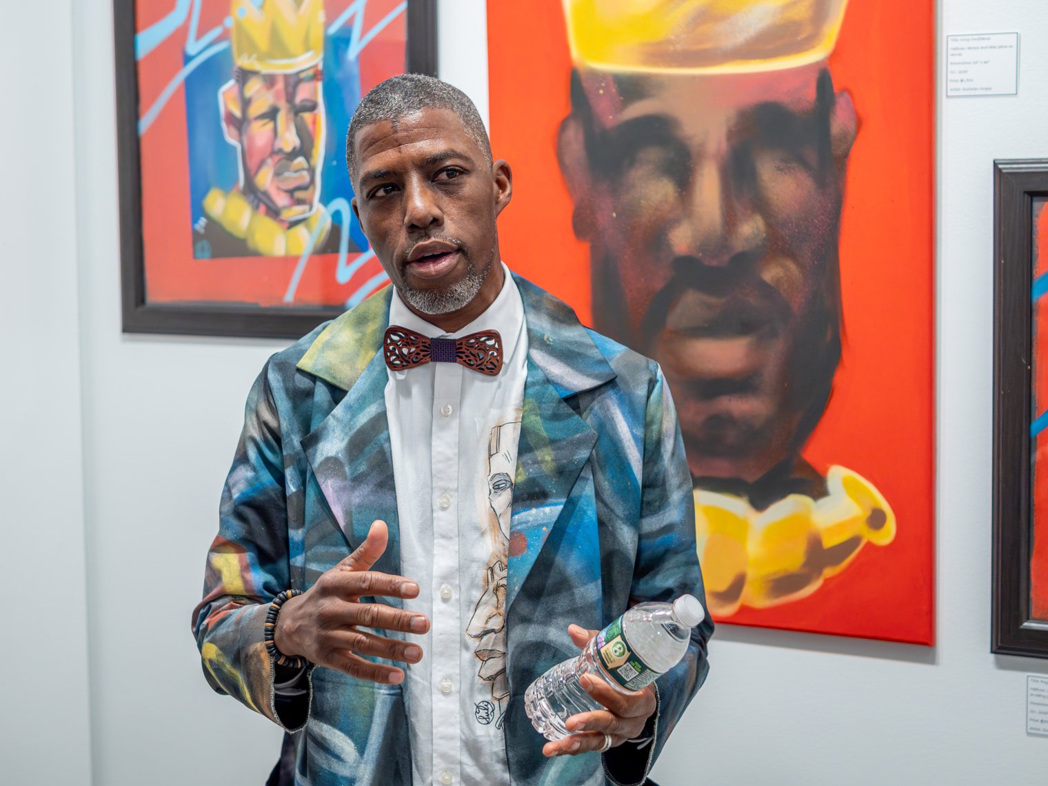 Man is pictured with a blue suit, red bow tie, holding a water bottle explaining something. 